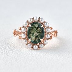 a close up of a ring with pearls and a green stone in the center on a white surface