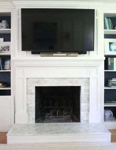 a tv mounted on the wall above a fireplace in a living room with built - in bookshelves