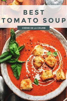 a bowl of tomato soup with bread croutons and basil leaves on the side