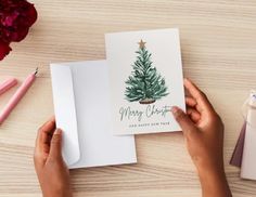 someone holding up a christmas card with a pine tree on it and the words merry christmas