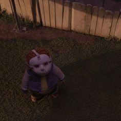 a creepy doll sitting in the grass next to a fence at night with its eyes closed