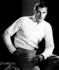 black and white photograph of a man in sweater sitting on the floor with his hands on his hips