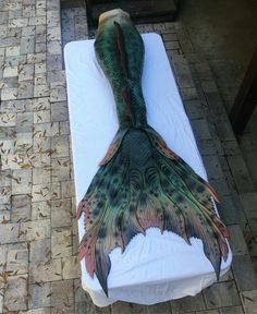 a mermaid tail laying on top of a white sheet covered cot with an orange and green pattern