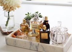 an assortment of perfumes in a marble tray on a white table with a flower