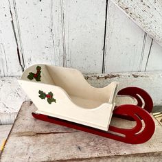 a white and red sleigh with holly decorations on the front sitting on a wooden table