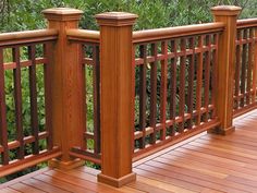 a wooden deck with railings and bushes in the background