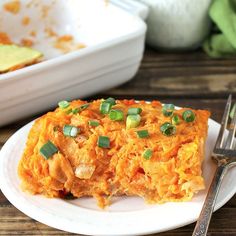 a white plate topped with an enchilada covered in cheese and green onions