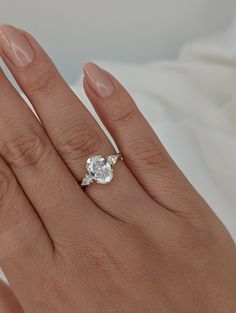 a woman's hand with a diamond ring on top of her finger and the other hand holding an engagement ring