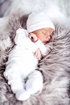 a baby is sleeping on top of a fur rug wearing a white hat and sweater