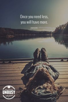 a person laying on top of a wooden dock next to a lake with the quote once you need less, you will have more