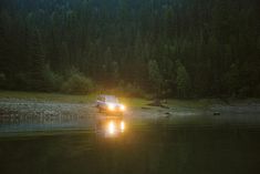 a car is driving through the water in the dark forest at night with its headlights on