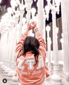 a woman standing in front of white columns and chandeliers with her hands up to the ceiling