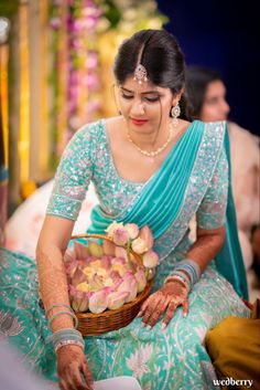 a woman in a blue sari holding a basket filled with flowers on her lap