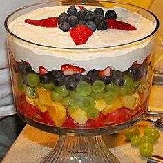 a fruit salad in a glass dish on top of a table with grapes and strawberries