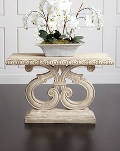 a vase with white flowers sitting on top of a wooden table next to a wall