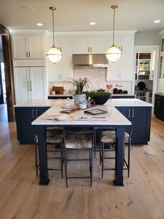 a large kitchen island with stools in front of it and lights hanging from the ceiling