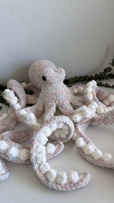 an octopus stuffed animal sitting on top of a white table next to some flowers and greenery