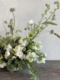 a glass vase filled with white flowers on top of a wooden table next to a wall