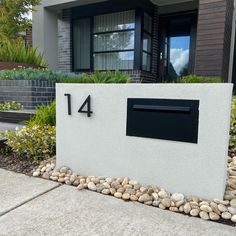 a house number sign in front of some plants and rocks on the sidewalk with a building behind it