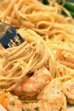 a fork full of pasta with shrimp and asparagus on the side in a white bowl