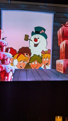 there is a snowman on the tv screen with other kids around it and presents