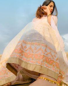 a woman sitting on top of a sandy beach wearing a white and pink dress with gold accents