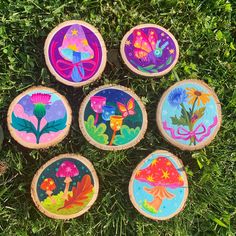 four painted wood slices sitting on top of grass next to each other in the shape of flowers