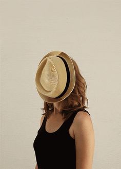 a woman wearing a hat and black tank top standing in front of a white wall