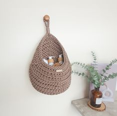 a crocheted bag hanging on the wall next to a vase with flowers in it