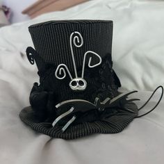 a black hat with white designs on it sitting on top of a bed next to a pillow