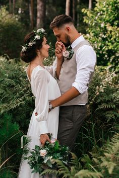 a bride and groom standing together in the woods with greenery on their wedding day