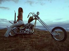 a woman sitting on top of a motorcycle in the middle of an open field with mountains in the background