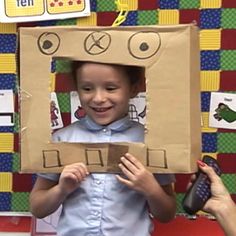 a young boy holding a cardboard box with an electronic device in it's head