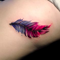 a colorful feather tattoo on the back of a woman's shoulder