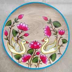 a decorative wooden plate with two swans surrounded by pink flowers and green leaves on a white tile floor