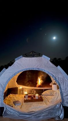 an outdoor tent set up with candles and food in it at night on the beach