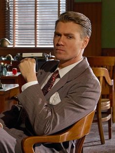 a man in a suit and tie sitting at a table with his hands on his hips