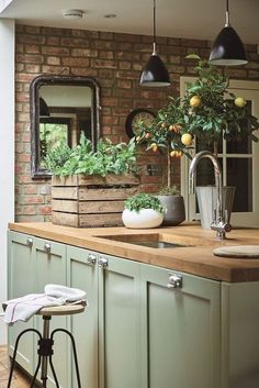 a kitchen with green cabinets and wooden counter tops next to a brick wall that has potted plants on it