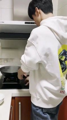 a young man cooking food on top of a stove next to a microwave in a kitchen