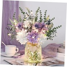 a vase filled with purple and white flowers on top of a table next to a cup