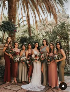 a group of women standing next to each other in front of a palm tree holding bouquets