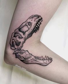 a black and white photo of a dinosaur skull tattoo on the right thigh, with an alligator's head in the middle