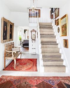 a staircase leading up to a living room with pictures on the wall and rugs