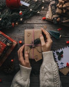 a person holding a wrapped present in front of christmas decorations and gifts on a wooden table