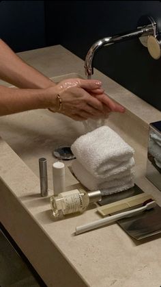 a person washing their hands in a bathroom sink with soap, toothbrushes and other items