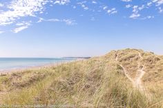 a sandy beach next to the ocean under a blue sky with wispy clouds