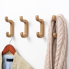 three wooden coat hooks hang on the wall next to a sweater and jacket hanging from it