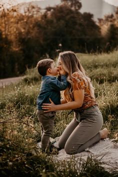 a mother kissing her son while sitting in the grass