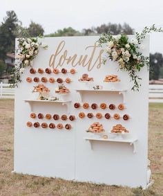 donuts are arranged on shelves in front of a sign with flowers and greenery