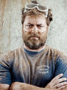 a bearded man with goggles on his head and arms crossed, standing in front of a concrete wall